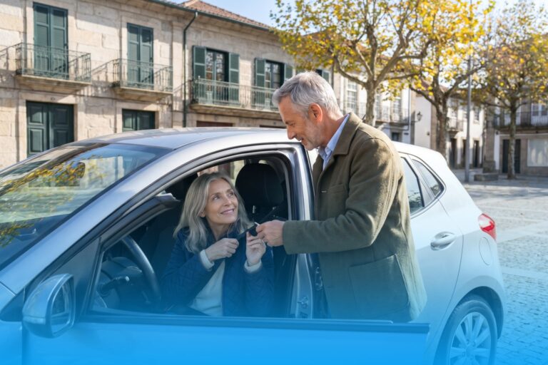 Woman in her early sixties at the wheel of a car on a square in the old town of Guimarães, her husband handing her the car key through the open driver door